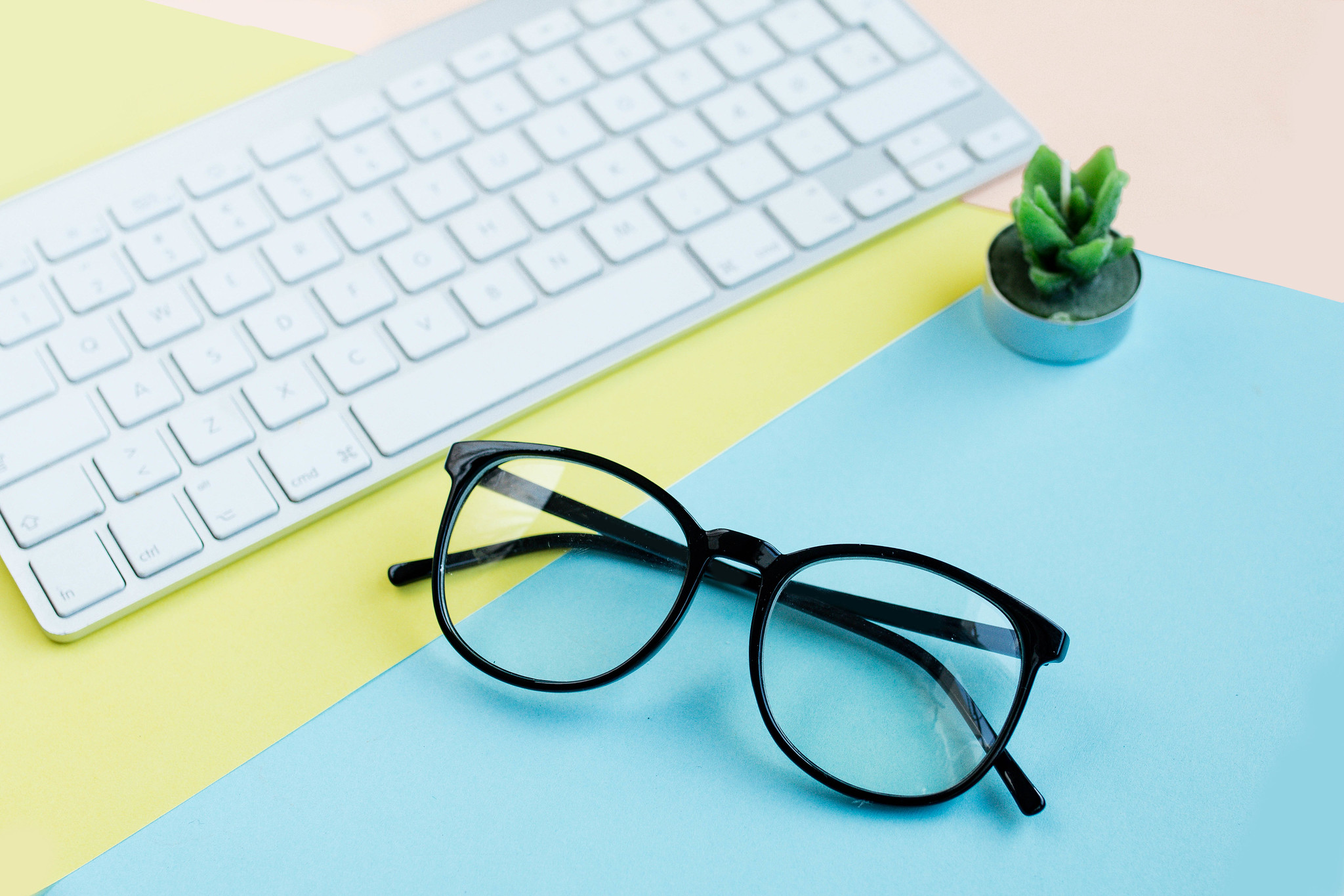 Flat lay with glasses, keyboard and cactus candle on colorful ba